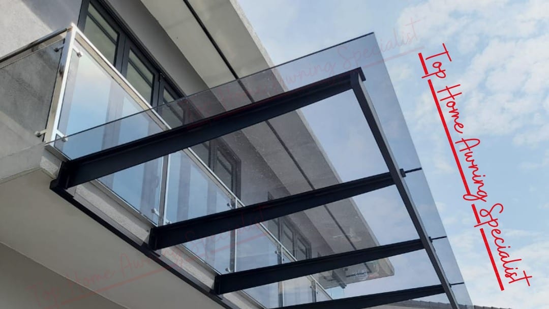 A glass awning seen from directly beneath, showing the black steel rafters, the tie rods and the glazing bars against a bright sky.