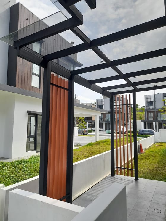 Looking up at a finished glass roof on a black steel frame over the driveway of a newly built terrace house, with wood-grain vertical fins to one side and clear sky through the glazing.