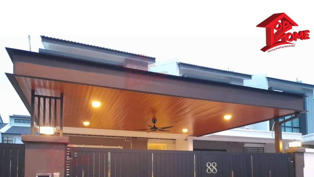 A wood-grain aluminium ceiling roof over a car porch at dusk with its downlights on and a ceiling fan turning beneath it.